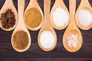 colheradas de diferentes tipos de açúcar em colheres de madeira alinhadas sobre superfície escura