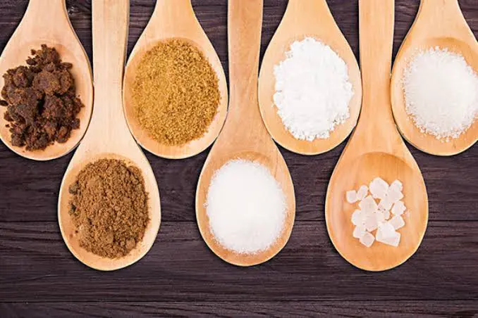 colheradas de diferentes tipos de açúcar em colheres de madeira alinhadas sobre superfície escura
