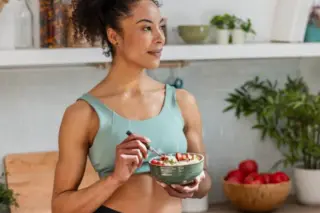 mulher jovem em uma cozinha segurando uma tigela com comida e comendo com uma colher