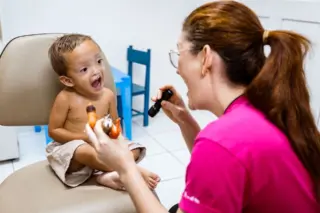 criança pequena com fissura no lábio sentada em cadeira durante consulta com profissional segurando lanterna e brinquedos