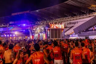 Público com abadás vermelhos reunido em frente a um trio elétrico iluminado dentro de um estádio