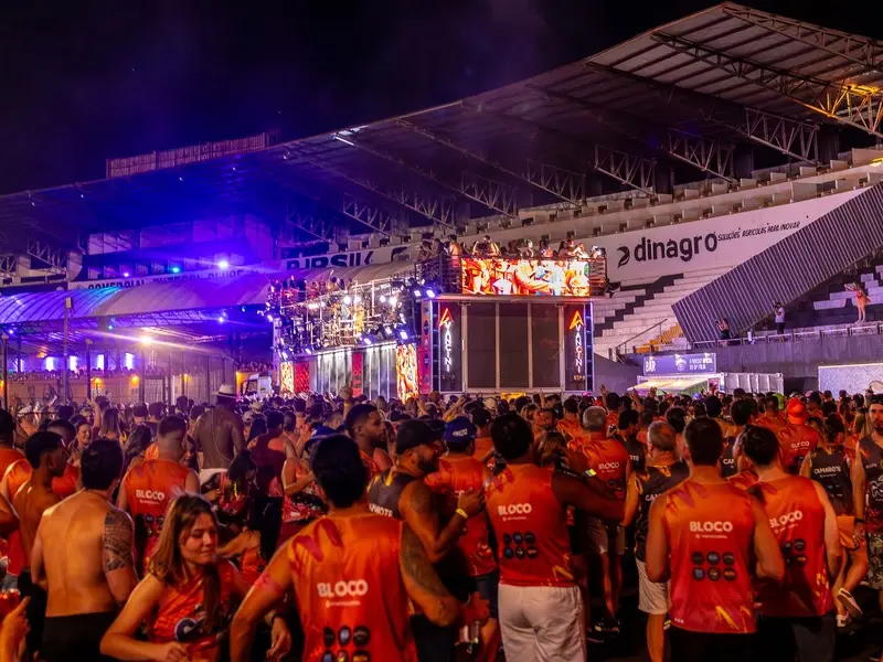 Público com abadás vermelhos reunido em frente a um trio elétrico iluminado dentro de um estádio