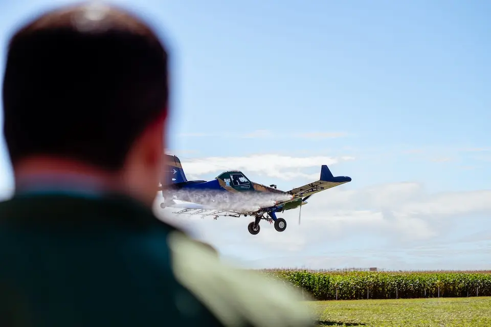 aeronave agrícola em voo baixo pulverizando com pessoa em primeiro plano desfocada