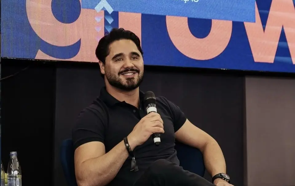 Profissional sentado segura microfone durante participação em evento de comunicação e marketing digital.