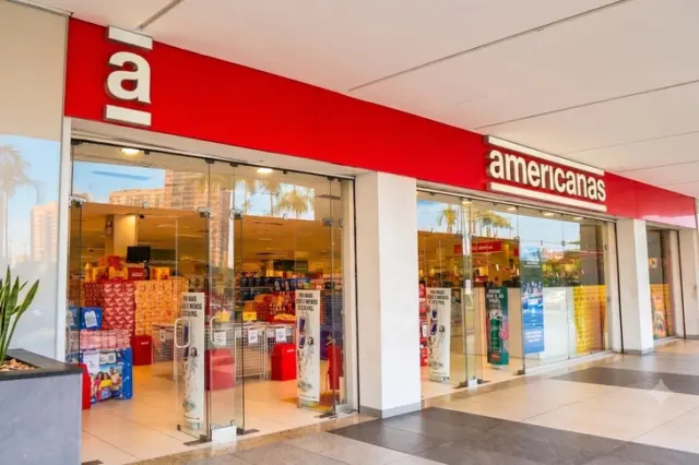 Fachada de loja Americanas com letreiro vermelho, portas de vidro e prateleiras visíveis no interior