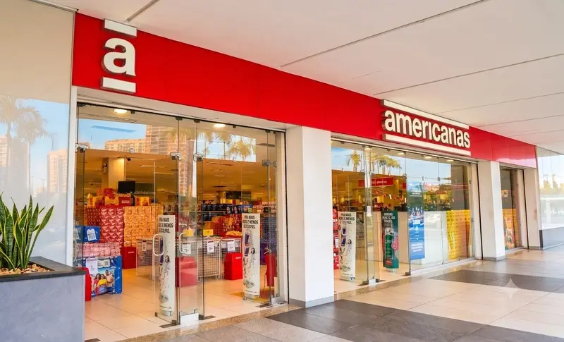 Fachada de loja Americanas com letreiro vermelho, portas de vidro e prateleiras visíveis no interior