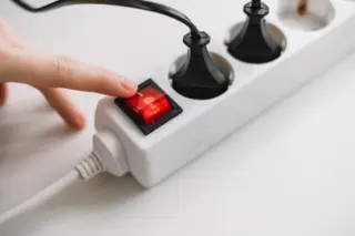 Dedo pressionando interruptor vermelho em régua de energia branca com cabos pretos conectados