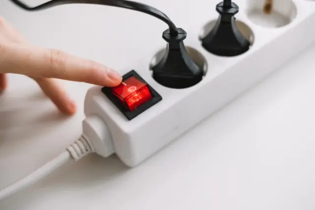 Dedo pressionando interruptor vermelho em régua de energia branca com cabos pretos conectados