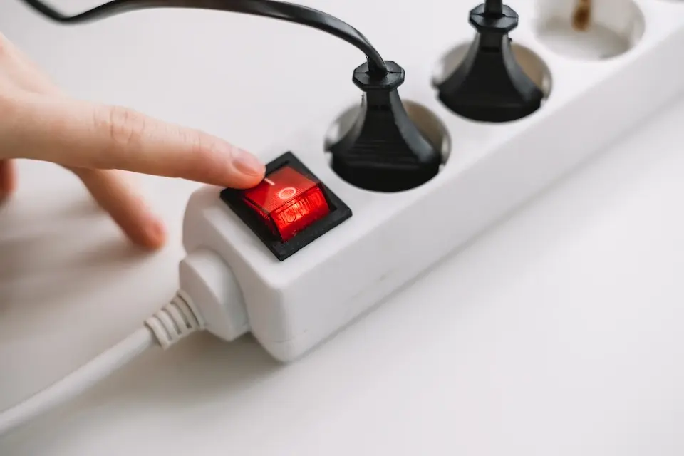 Dedo pressionando interruptor vermelho em régua de energia branca com cabos pretos conectados