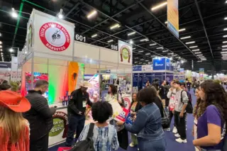 Estande de feira com pessoas reunidas, balcão com logotipos da Festa do Peão de Barretos e placas numeradas no pavilhão