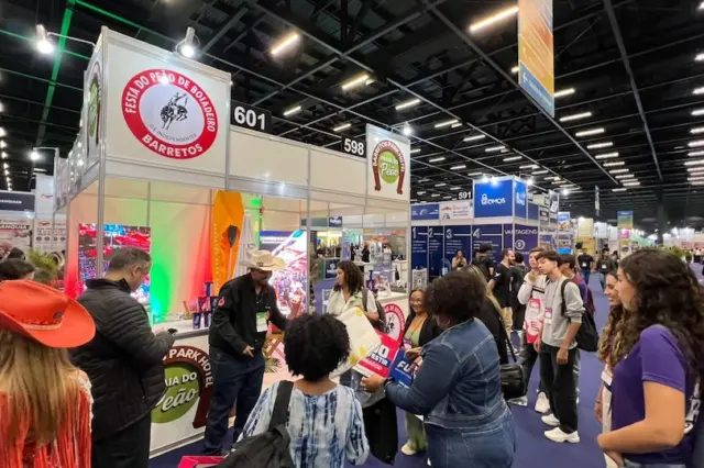 Estande de feira com pessoas reunidas, balcão com logotipos da Festa do Peão de Barretos e placas numeradas no pavilhão