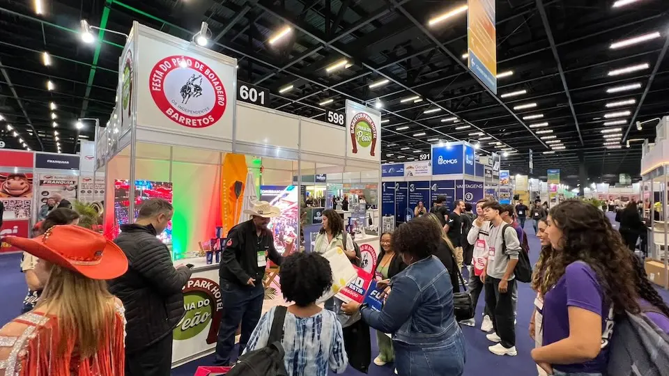 Estande de feira com pessoas reunidas, balcão com logotipos da Festa do Peão de Barretos e placas numeradas no pavilhão