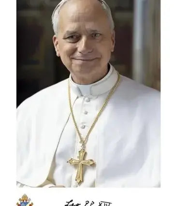 Homem idoso com batina branca e crucifixo dourado ao peito, sorrindo levemente, fundo interno desfocado