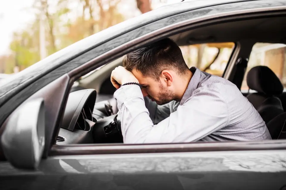 homem sentado no banco do motorista com a cabeça apoiada nos braços sobre o volante