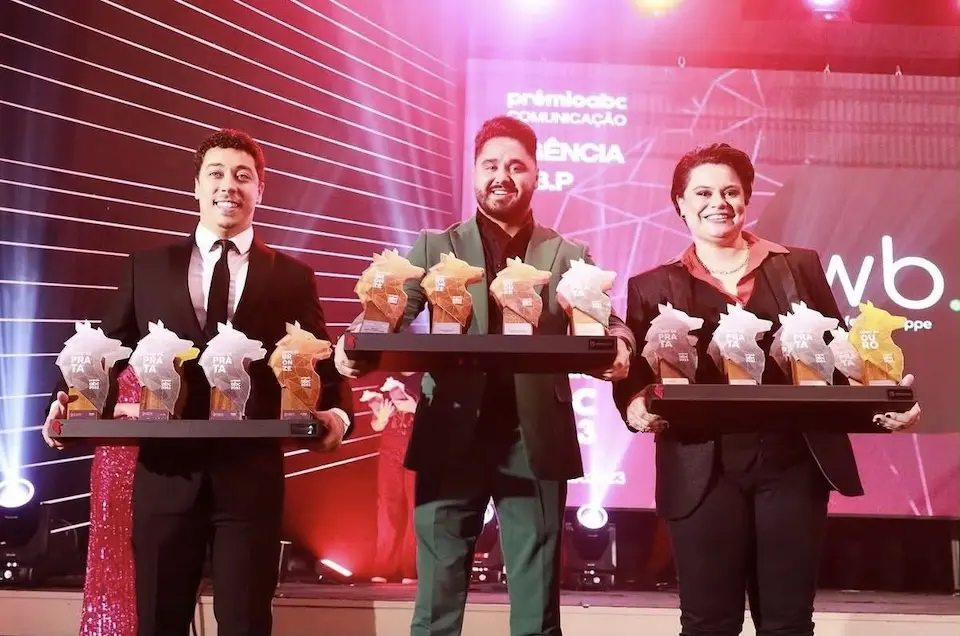 Três profissionais exibem troféus durante cerimônia de premiação do setor de comunicação.