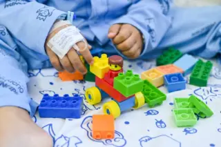 mãos de criança com curativo segurando blocos de montar plásticos coloridos sobre lençol estampado