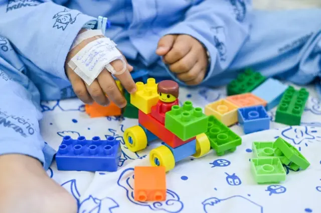 mãos de criança com curativo segurando blocos de montar plásticos coloridos sobre lençol estampado