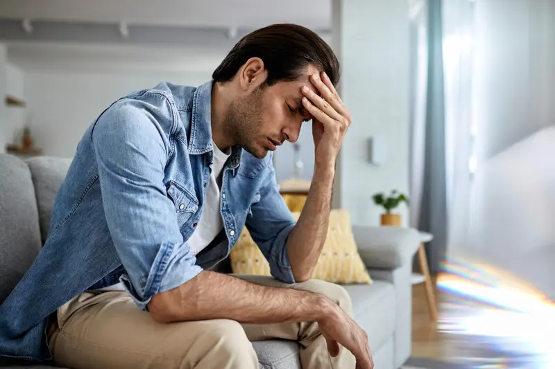 Homem sentado no sofá com a mão na testa e expressão de preocupação