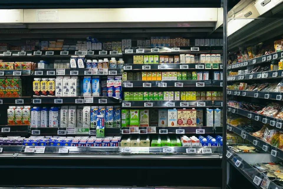 prateleiras refrigeradas de supermercado com embalagens de leite, bebidas e produtos lácteos e etiquetas de preço