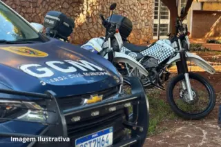 Viatura azul da Guarda Civil Municipal com letras "GCM" no capô e duas motocicletas brancas com padrão quadriculado estacionadas