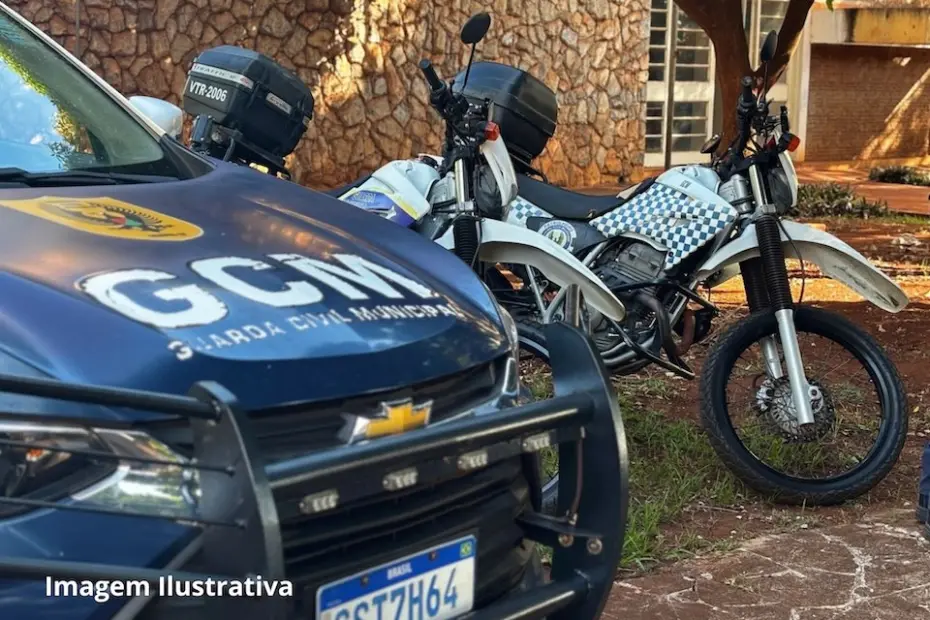 Viatura azul da Guarda Civil Municipal com letras "GCM" no capô e duas motocicletas brancas com padrão quadriculado estacionadas