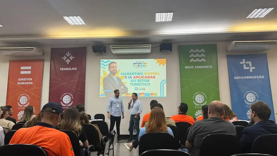 Plateia sentada de costas observa dois palestrantes no palco com telão sobre marketing digital e IA e faixas verticais temáticas nas laterais