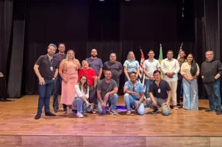 Grupo de pessoas posando em palco com bandeiras e cortina preta ao fundo