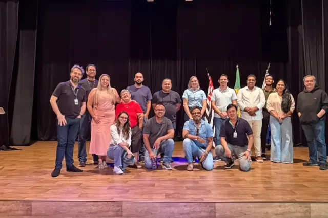 Grupo de pessoas posando em palco com bandeiras e cortina preta ao fundo