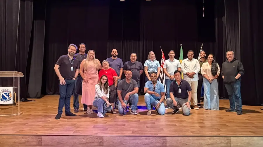 Grupo de pessoas posando em palco com bandeiras e cortina preta ao fundo