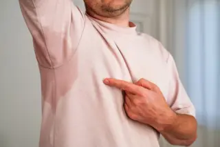 Pessoa levantando o braço e mostrando uma mancha de suor grande na axila da camiseta rosa