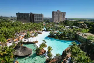 vista aérea de complexo aquático com grandes piscinas, palmeiras, espreguiçadeiras e prédios de hotel ao fundo