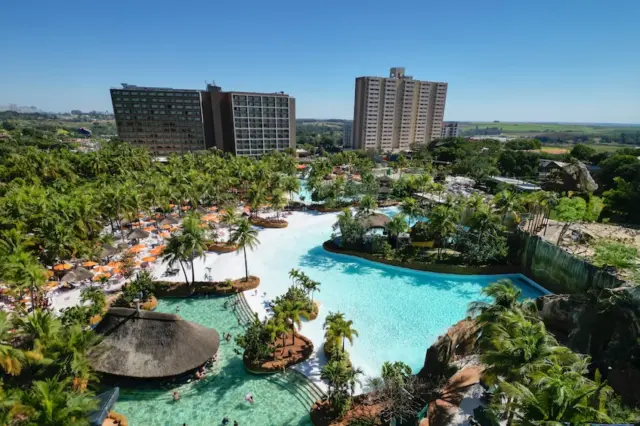 vista aérea de complexo aquático com grandes piscinas, palmeiras, espreguiçadeiras e prédios de hotel ao fundo