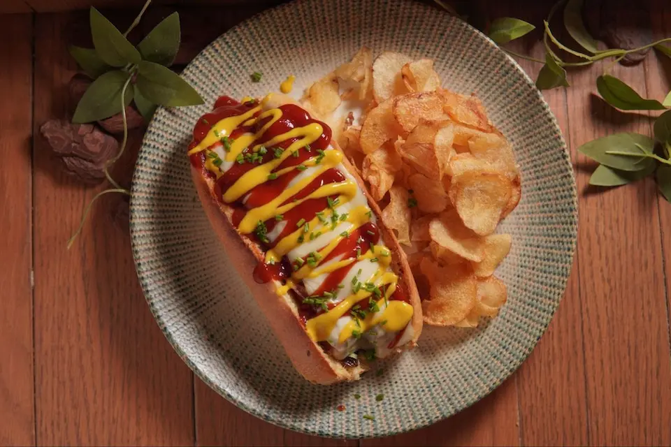 cachorro-quente em pão com coberturas de ketchup, maionese e mostarda, acompanhado de chips