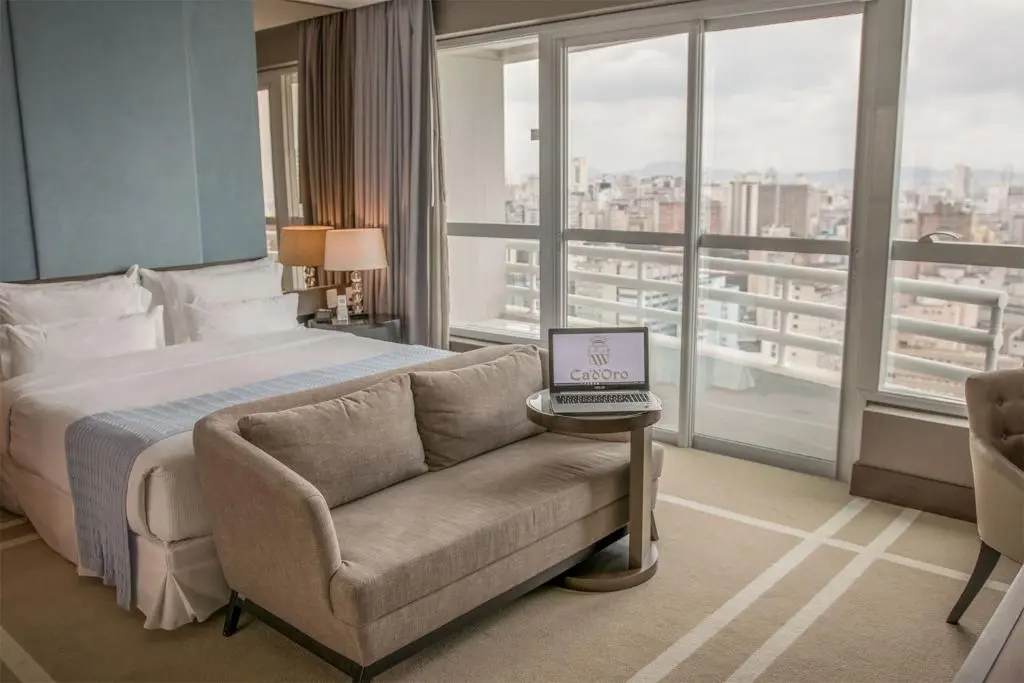 Quarto de hotel com cama, mesa de madeira e vista para a cidade e mar pela janela