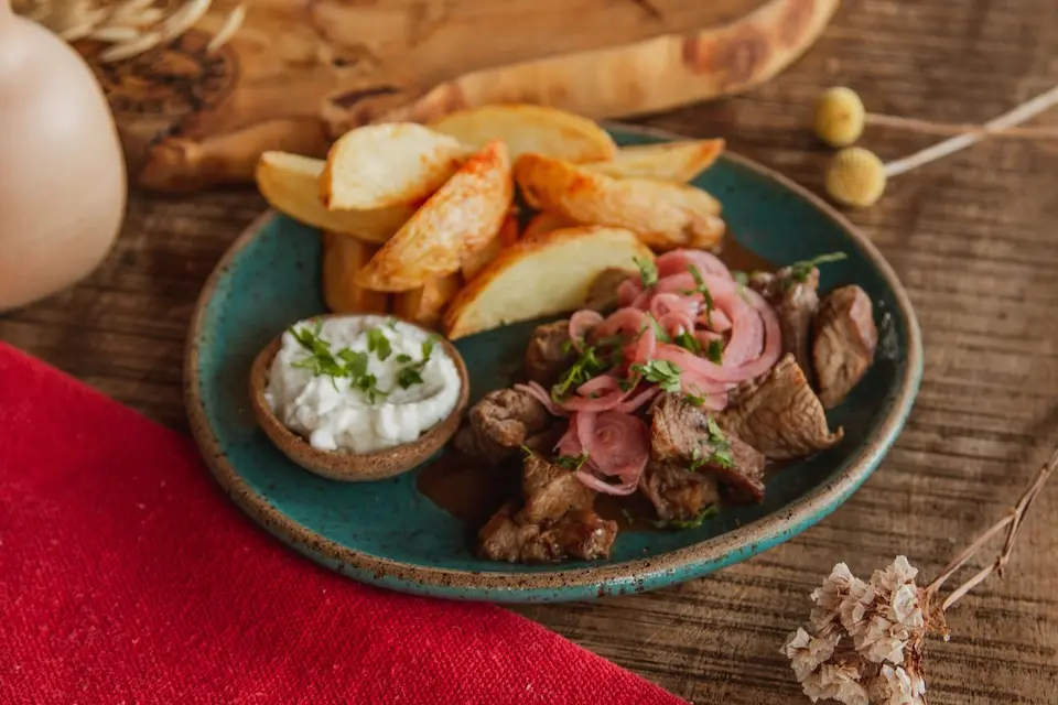 prato com pedaços de carne grelhada, cebolas em conserva, batatas rústicas e molho branco