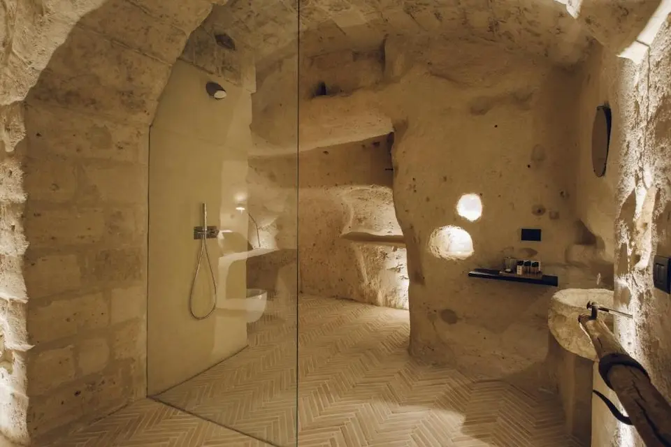 quarto com cama de madeira e banco-cama, paredes brancas e adereços de palha