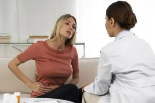 mulher sentada com a mão sobre o abdômen conversando com médica de jaleco