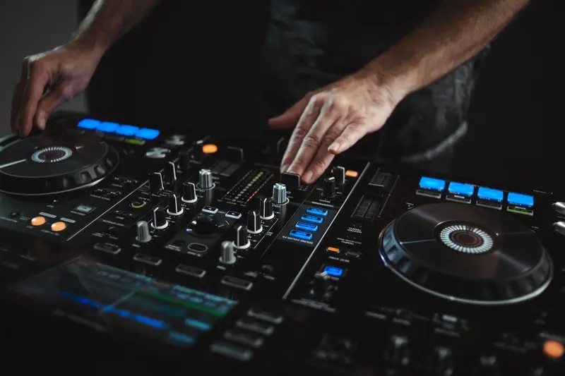 Mãos de um DJ ajustando controles em uma mesa de mixagem com botões iluminados