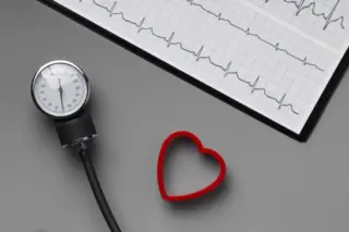 manômetro de esfigmomanômetro, um objeto em forma de coração vermelho e um registro de eletrocardiograma sobre fundo cinza