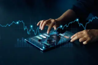 Mãos de uma pessoa interagindo com um tablet exibindo painéis e ícones, com gráficos e uma linha de tendência financeira azul sobreposta