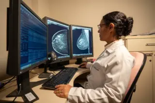 profissional de saúde sentada diante de monitores com imagens de mamografia