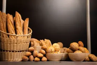 Cesta de vime com baguetes, tigelas com pães variados e pequenos pães sobre balcão, fundo preto