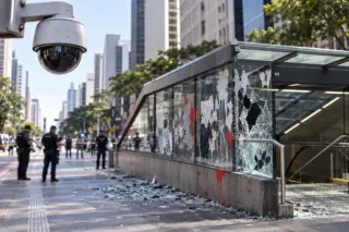 Câmera de segurança monitora área com vidros quebrados e sinais de vandalismo em entrada de metrô, em ilustração da Avenida Paulista.