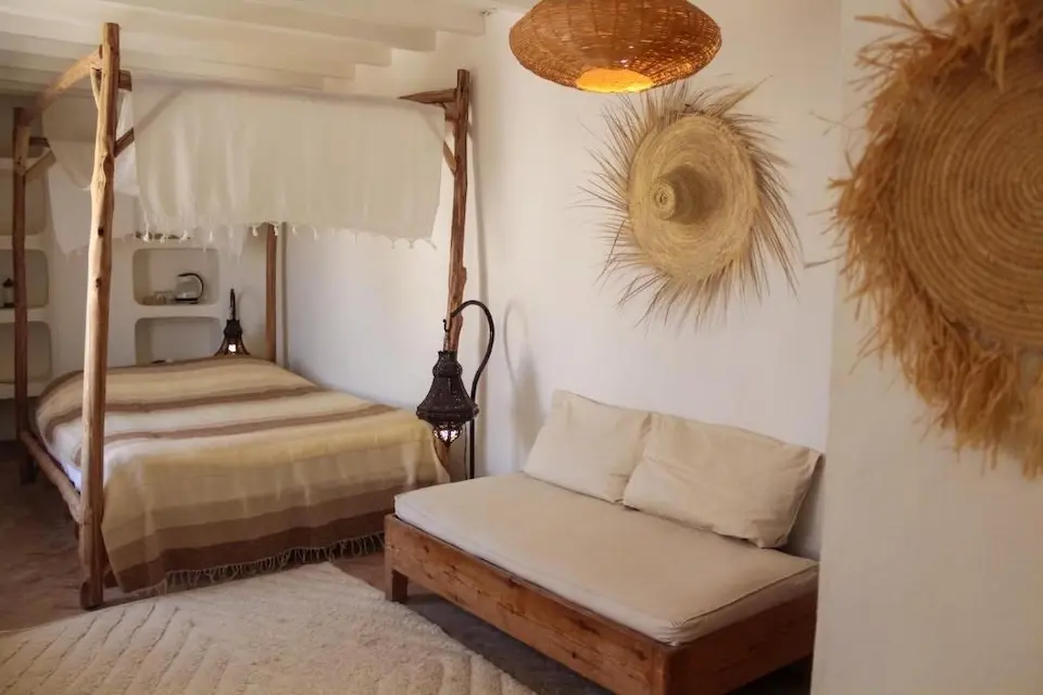 quarto claro com cama de dossel, sofá de madeira e objetos de palha na parede