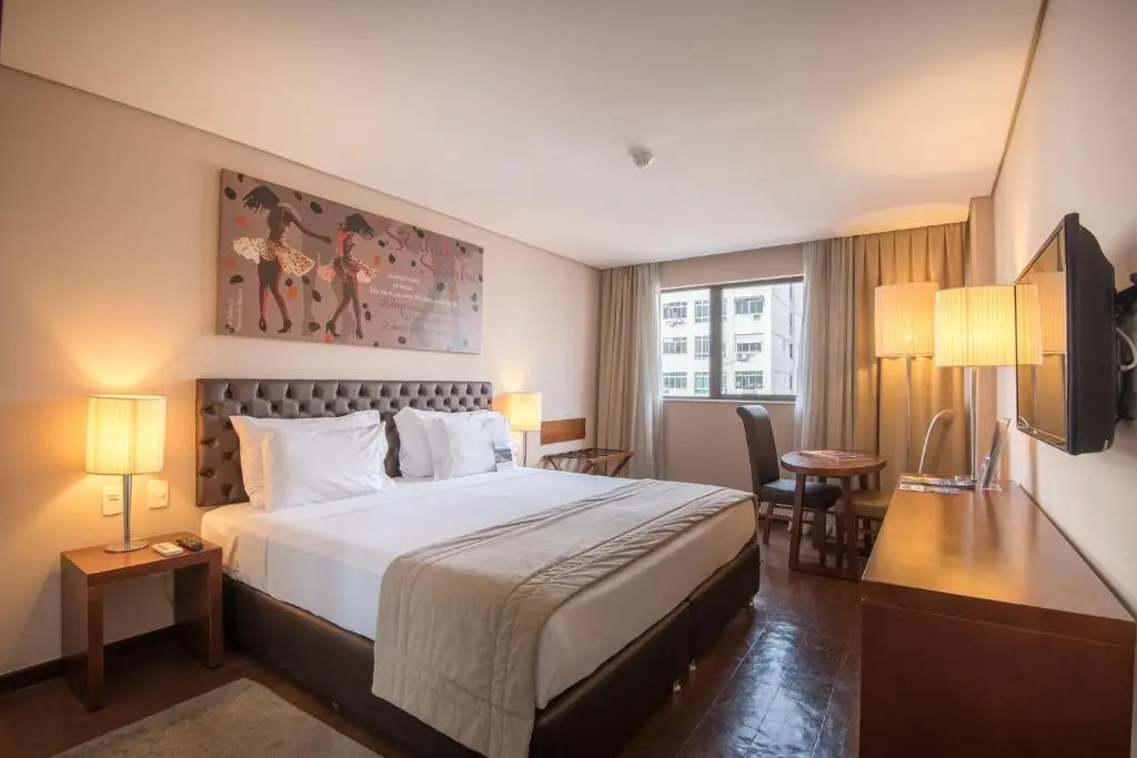 Quarto de hotel com cama de casal, quadro decorativo e iluminação amarelada