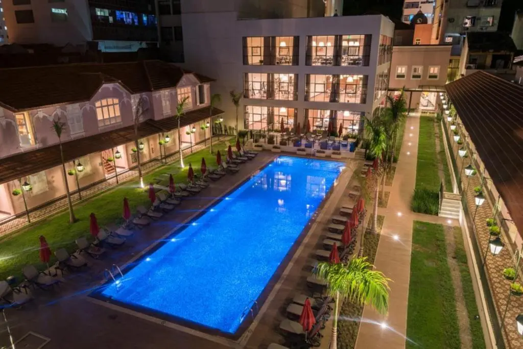 Piscina externa iluminada à noite em pátio de hotel com espreguiçadeiras