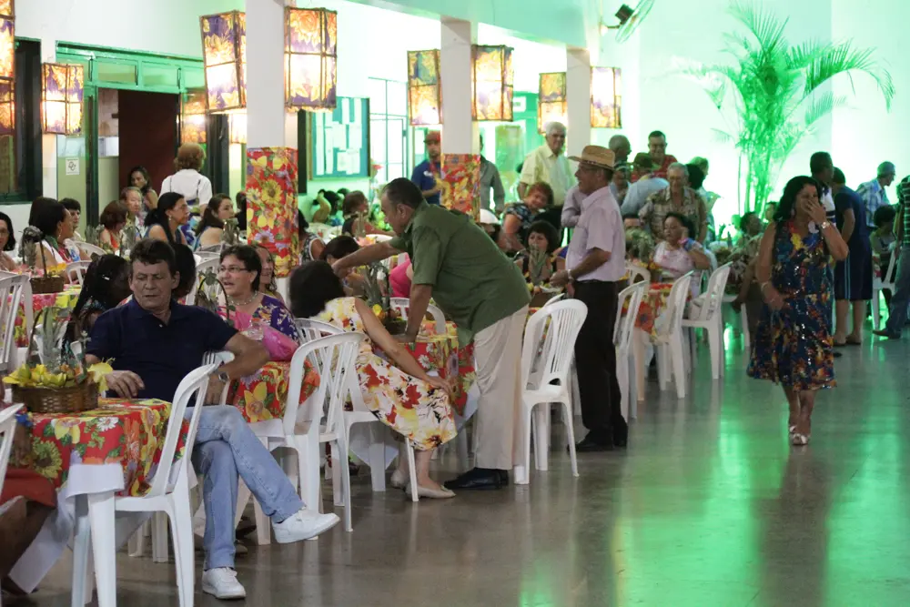 Mesas arrumadas com toalhas floridas e convidados sentados e conversando