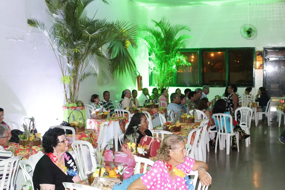 Fila de mesas com convidados sentados sob iluminação verde e plantas decorativas