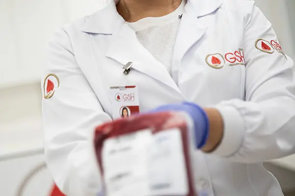 profissional de saúde com jaleco branco do GSH segurando uma bolsa de sangue com etiqueta
