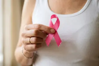 Mãos segurando um laço rosa de conscientização do câncer de mama sobre uma camiseta branca